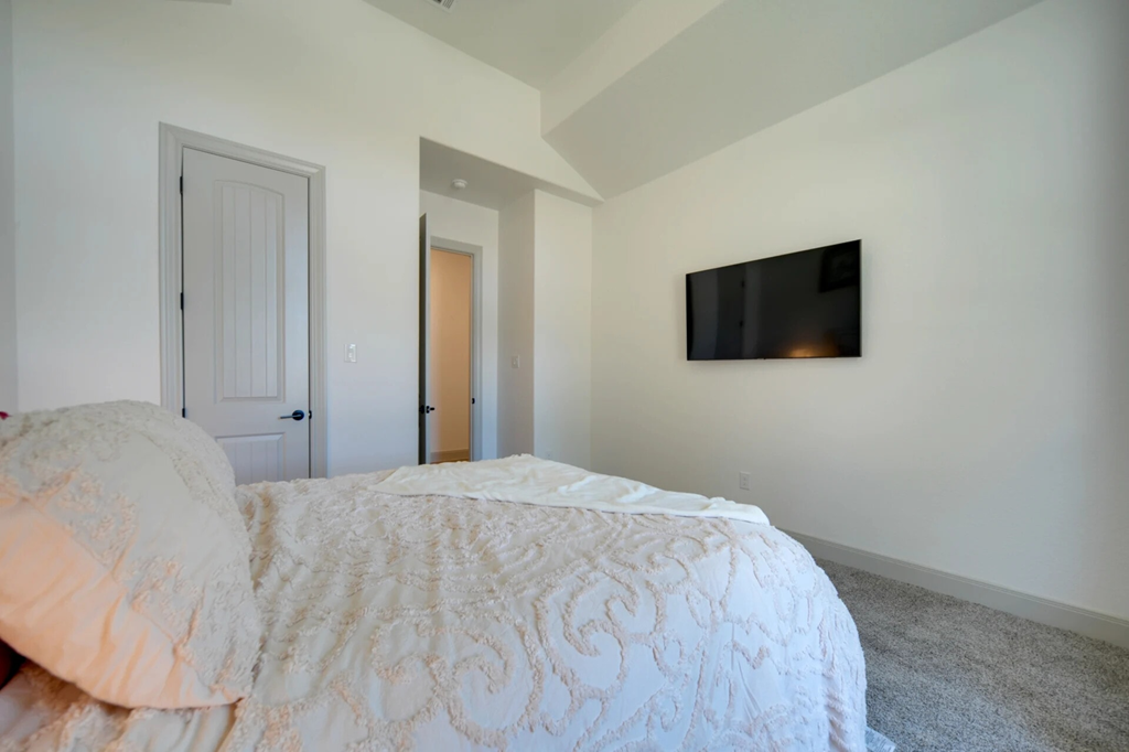 A bedroom with a bed, a door, and a television mounted on the wall.