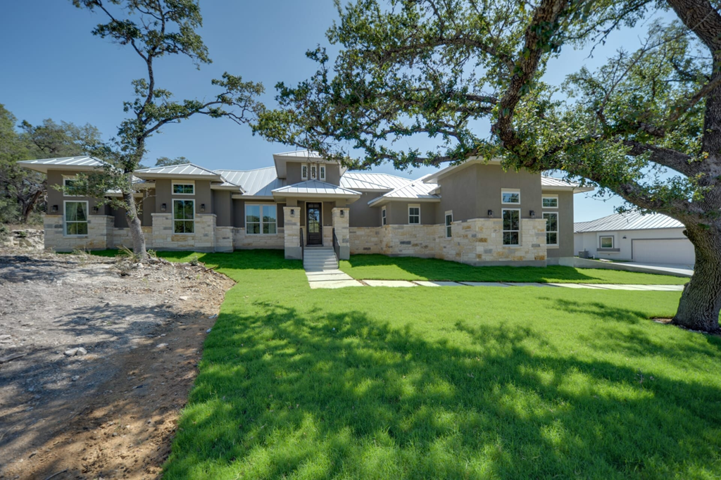 A modern house with a green lawn and trees in the background.