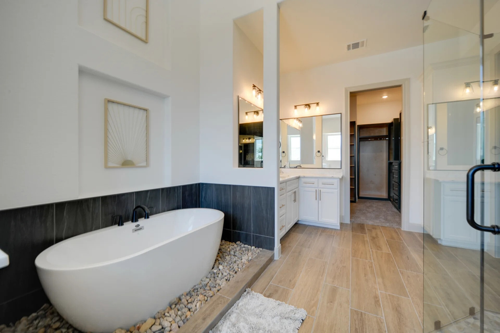A white freestanding bathtub sits in a bathroom with a wooden floor and a white rug.