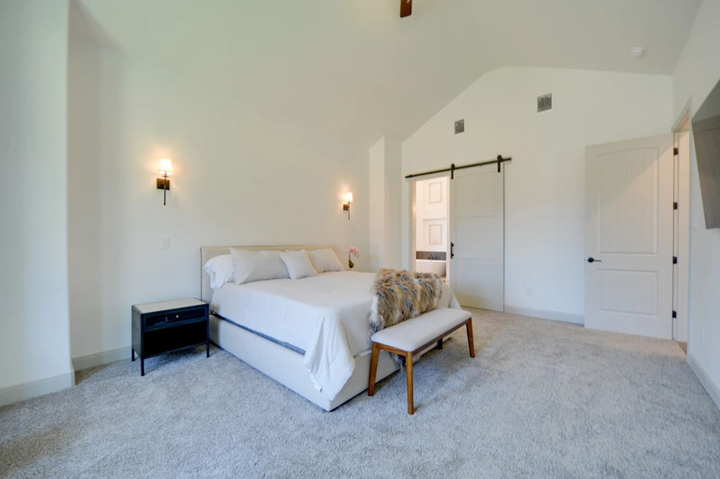 A bedroom with a bed, bench, and two wall sconces.