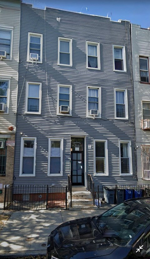 A grey building with a black car parked in front.