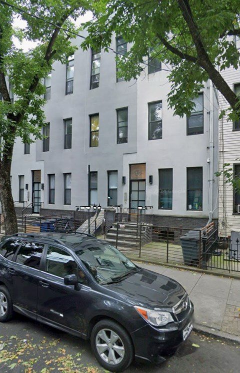 A black car is parked on the sidewalk in front of a white building.
