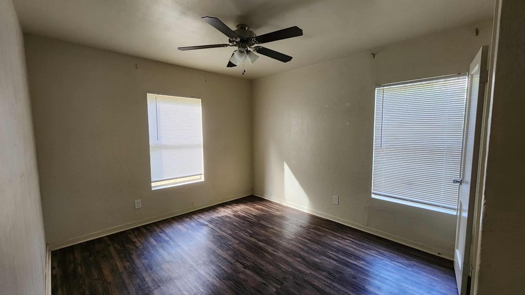 A room with a ceiling fan and two windows.