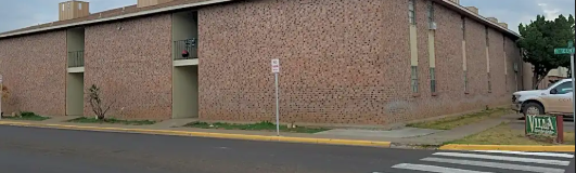 A building with a brick wall and a white car parked in front.