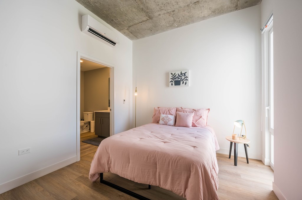 A bedroom with a pink bedspread and a painting on the wall.