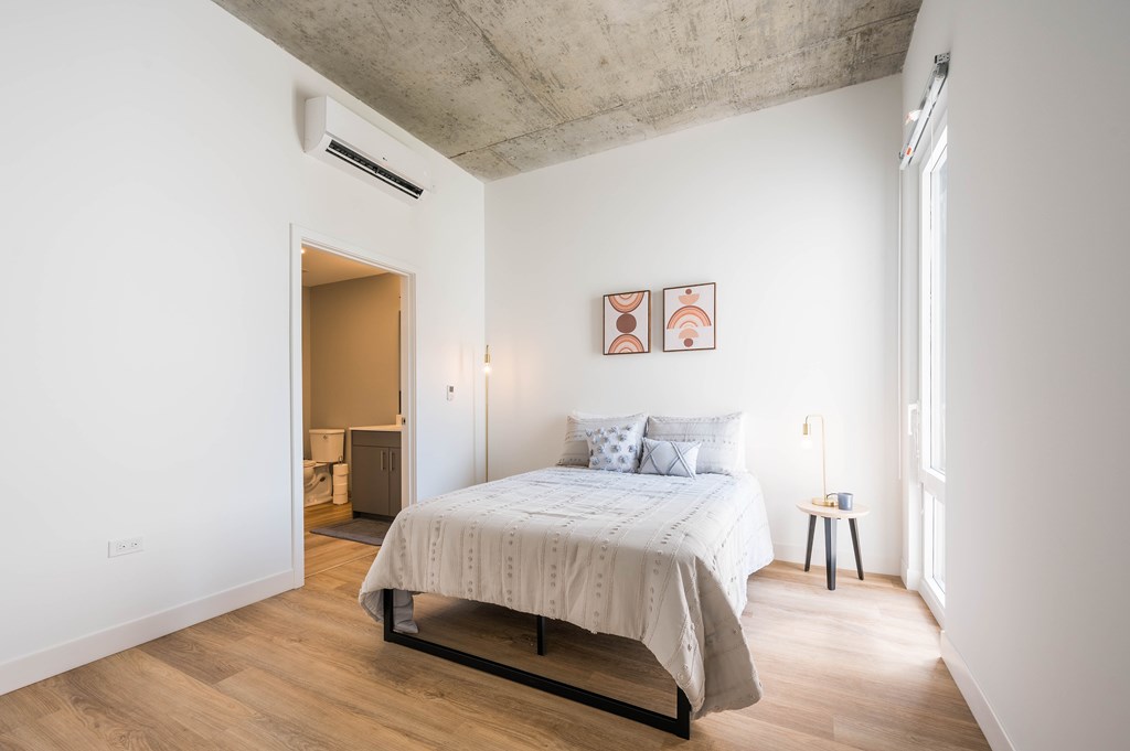 A bedroom with a bed, nightstand, and a window.