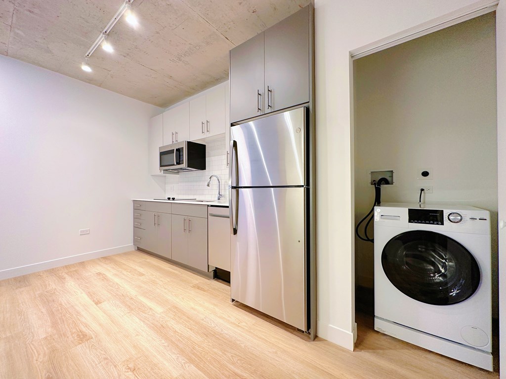 A modern kitchen with a refrigerator, microwave, and washing machine.