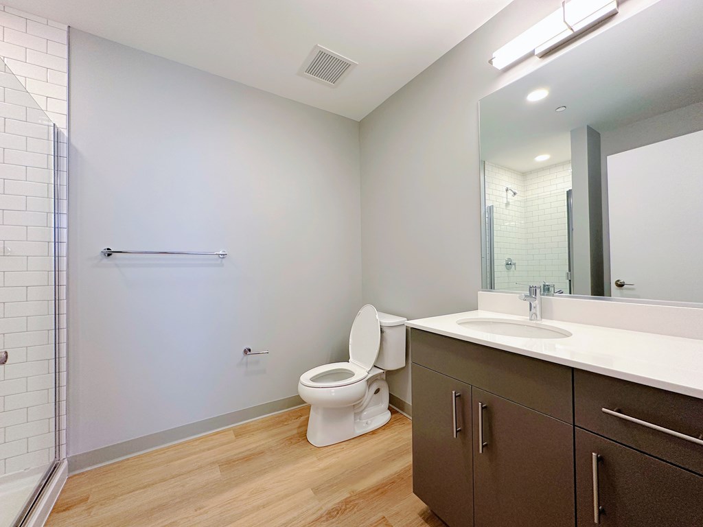 A white toilet sits in a bathroom with a wooden floor and a white sink.