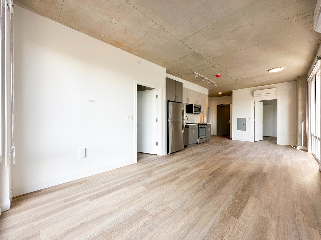 A spacious room with wooden flooring and a kitchen area in the background.