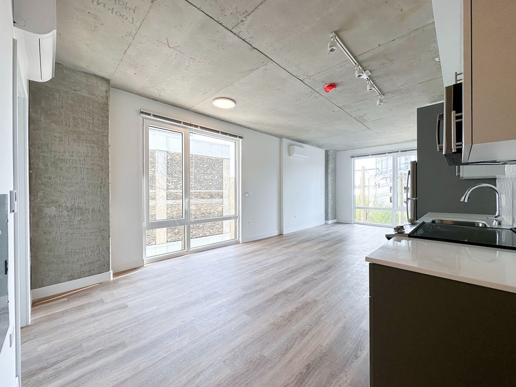 A room with a wooden floor and a kitchen area with a microwave.