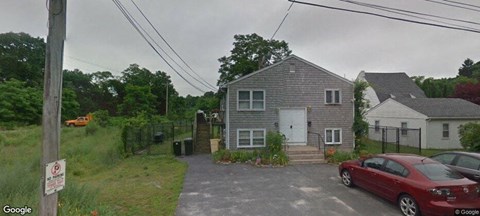 A grey house with a red car parked in front.