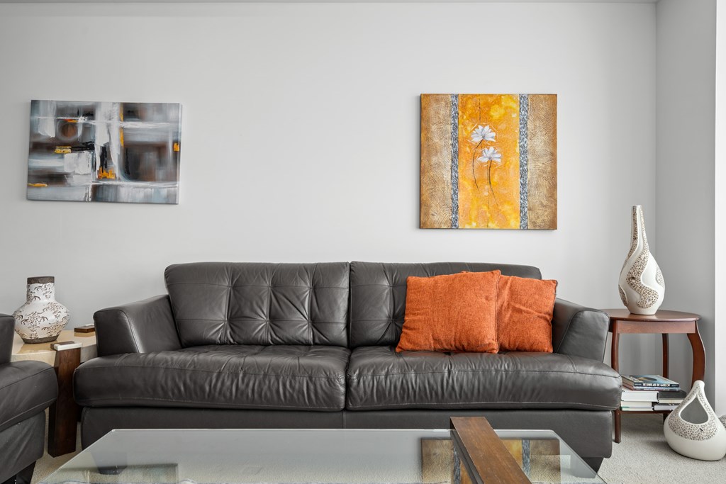 A grey couch with an orange pillow and a painting on the wall.