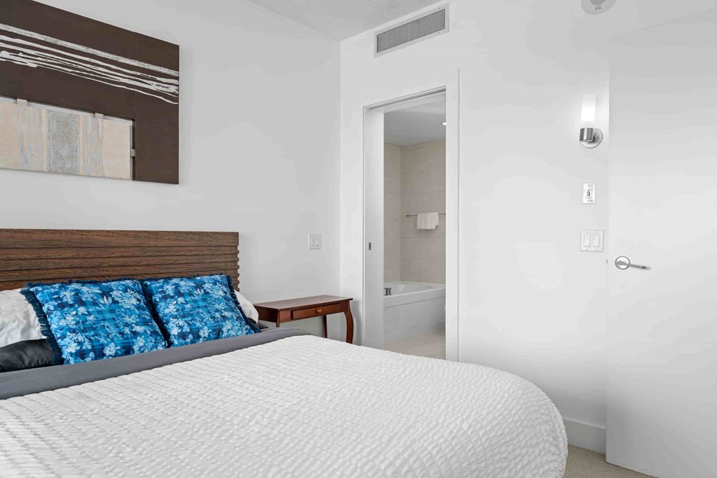 A bed with a white comforter and two blue patterned pillows.