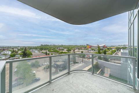 A balcony with a glass railing overlooks a parking lot and buildings.