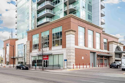 A modern glass building sits behind a red brick building with cars parked in front.