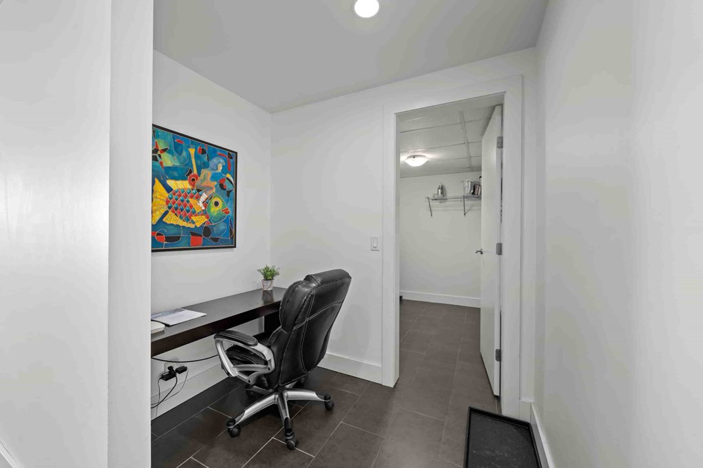 A room with a desk and a chair with a painting on the wall.