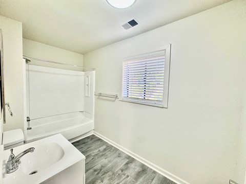 A white bathroom with a sink, mirror, and bathtub.