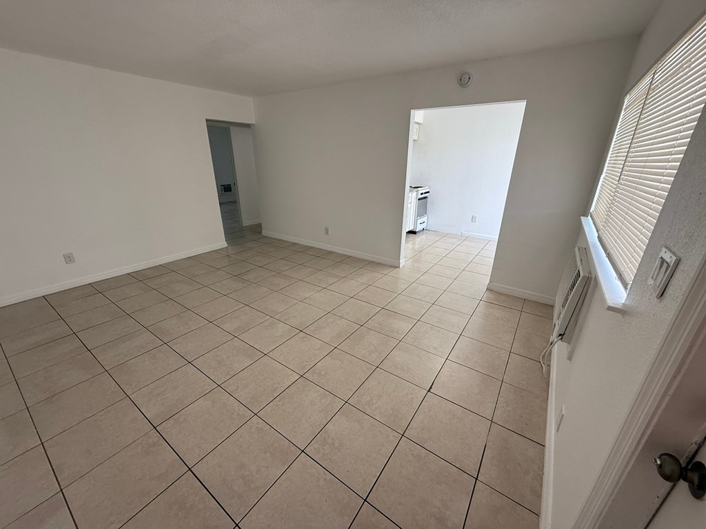 A room with white walls and tiled flooring with a door on the left and a window on the right.