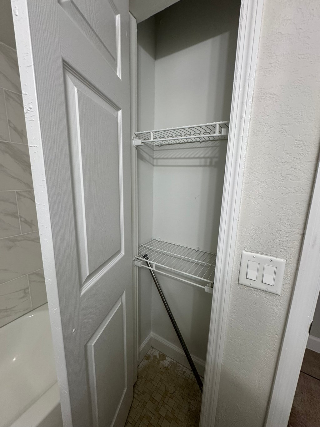 A white closet with a white bathtub in the background.