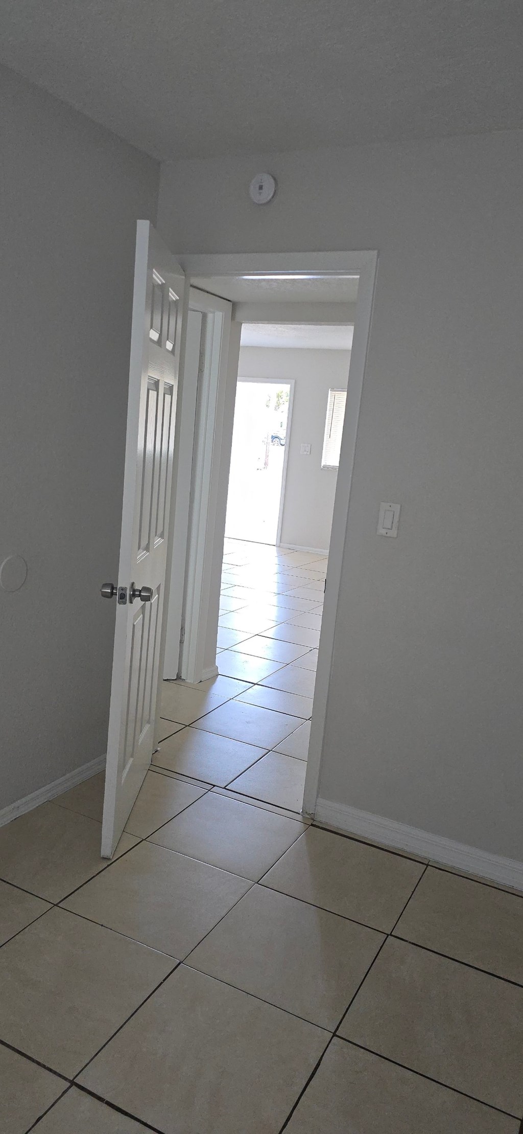 A hallway with a white door and tiled floor.