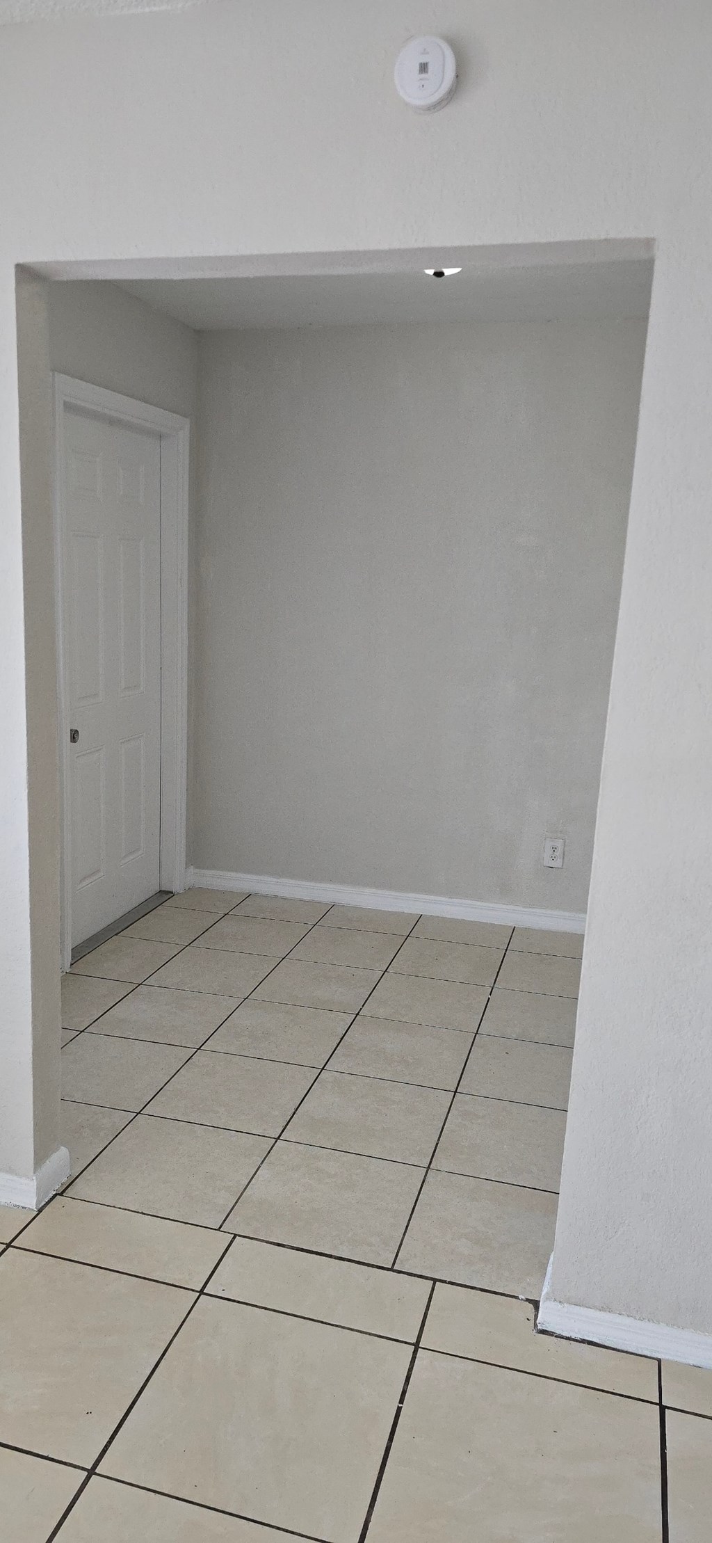 A white door is in a white room with a smoke detector on the ceiling.