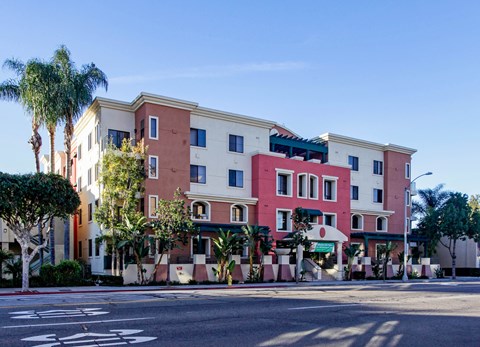A multi-story building with a red and beige facade is surrounded by palm trees.