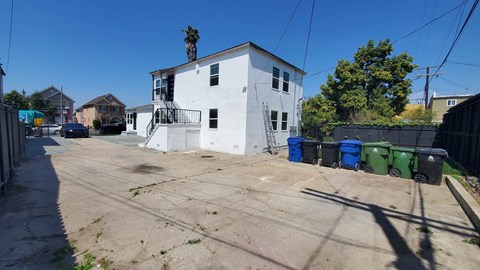 A white building with a blue and green trash bins in front.