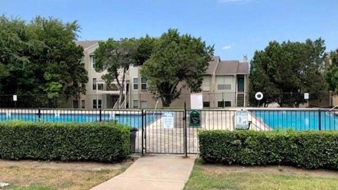 A pool surrounded by a black fence and green bushes.