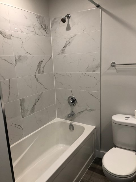 A white toilet sits next to a bathtub in a bathroom with marble tile walls.