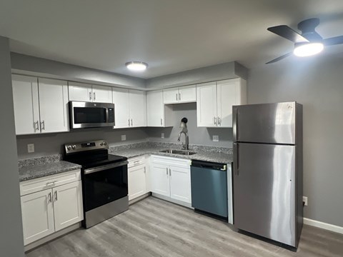 A kitchen with a stainless steel refrigerator, black stove, and white cabinets.