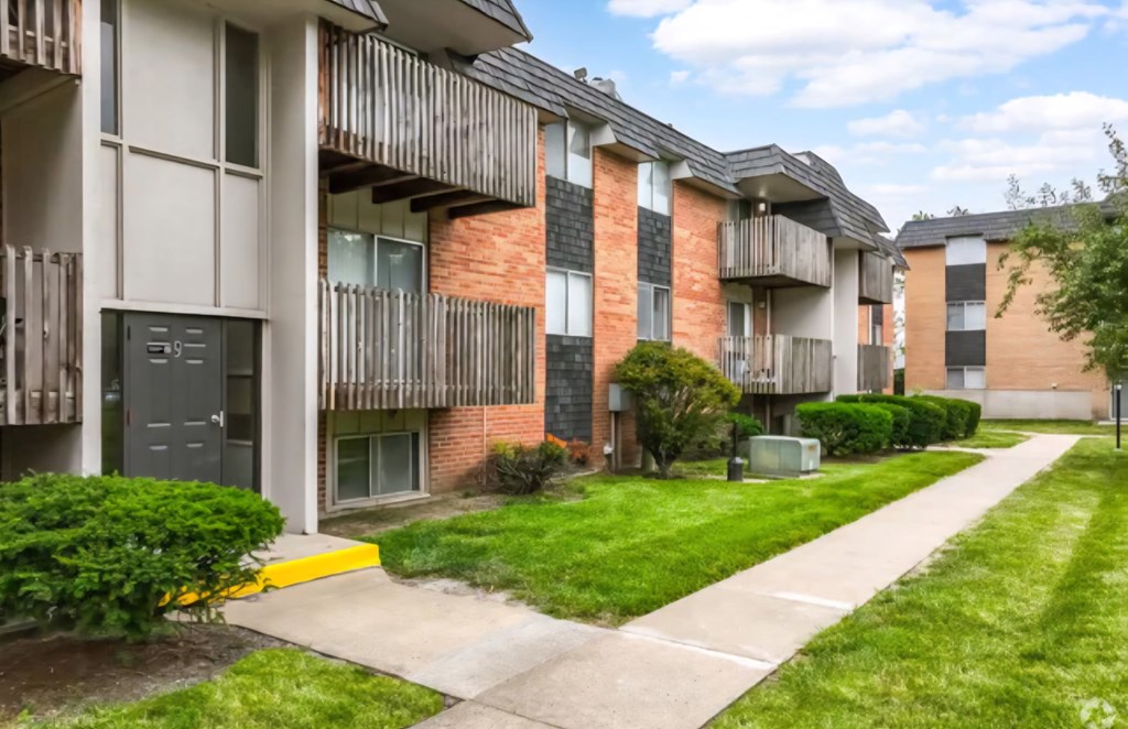 Apartment building with a green lawn and sidewalk in front.
