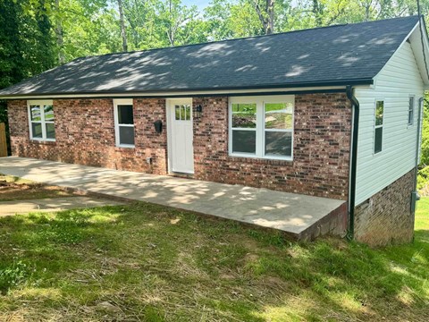 A small house with a white door and windows is surrounded by grass and trees.