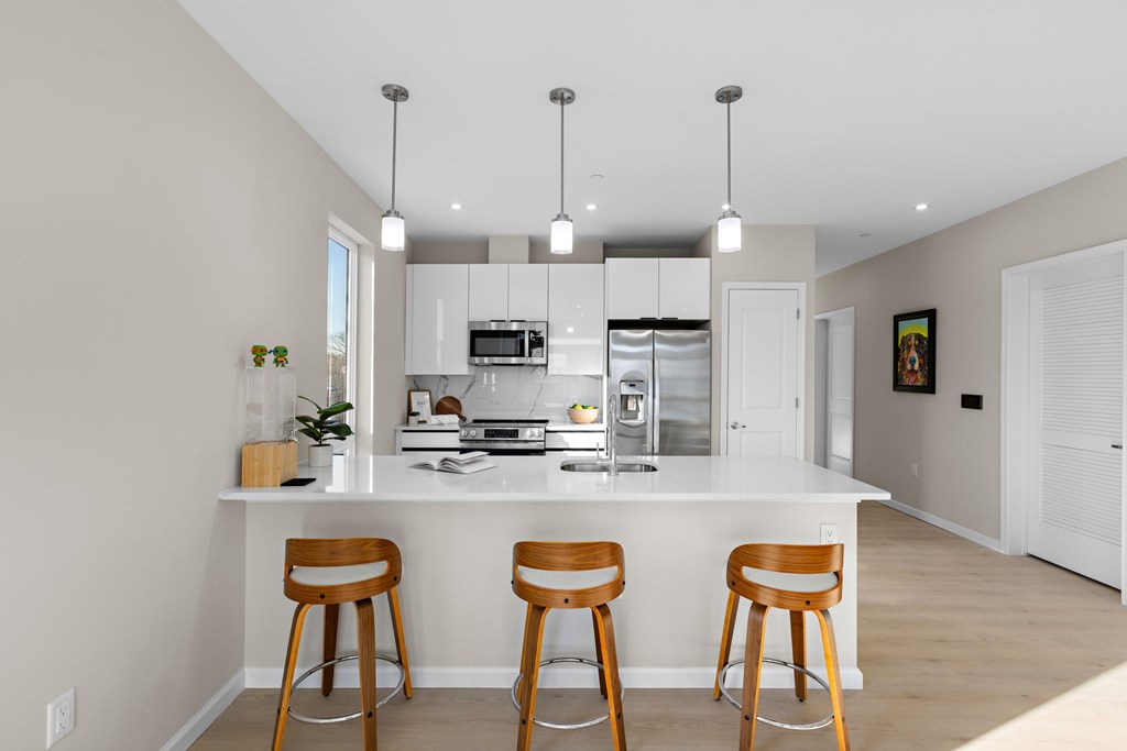 A kitchen with a white countertop and wooden bar stools.