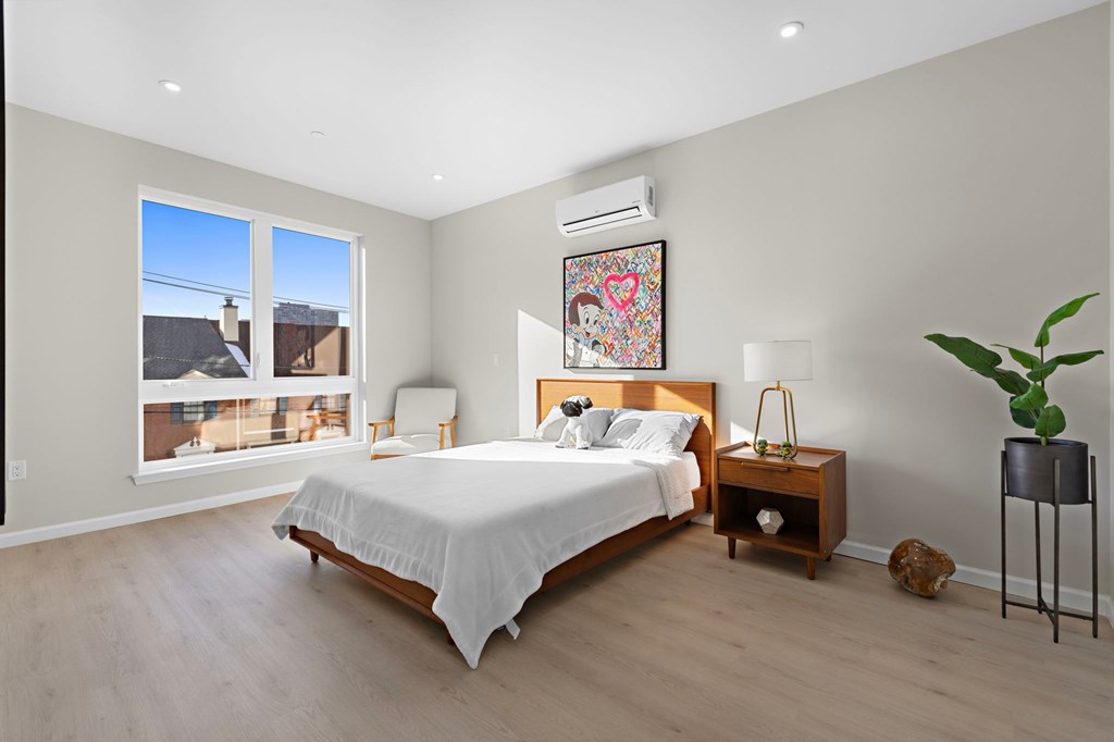 A bedroom with a large bed, a chair, a nightstand, and a plant.