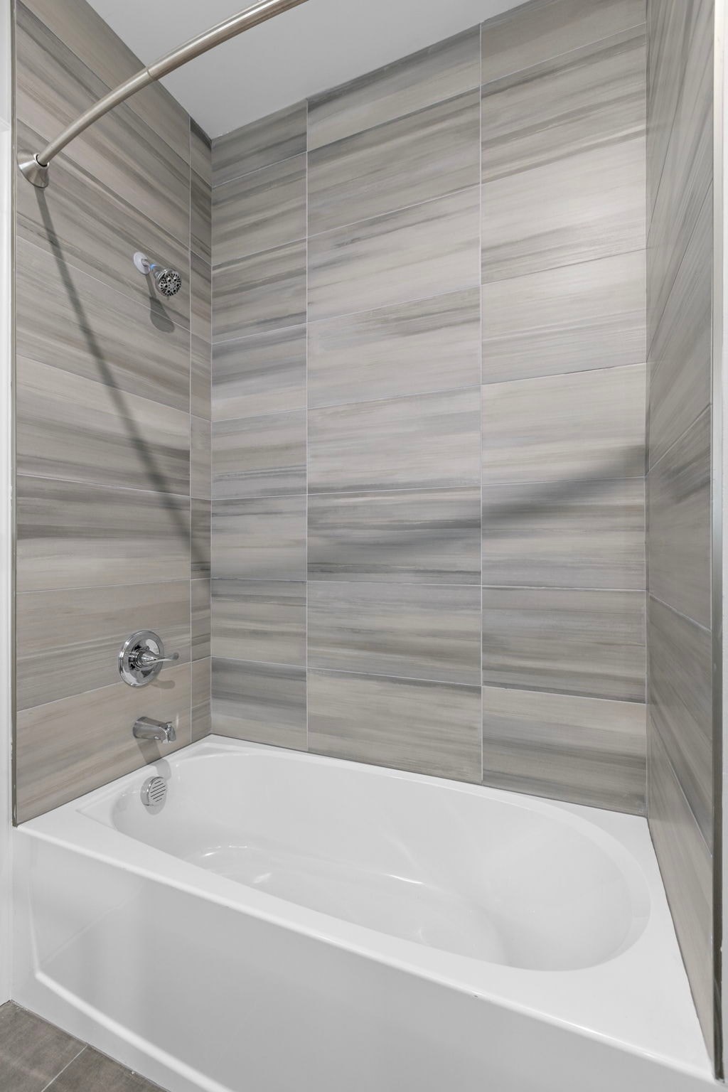 A white bathtub with a shower head and a wall of tiles.