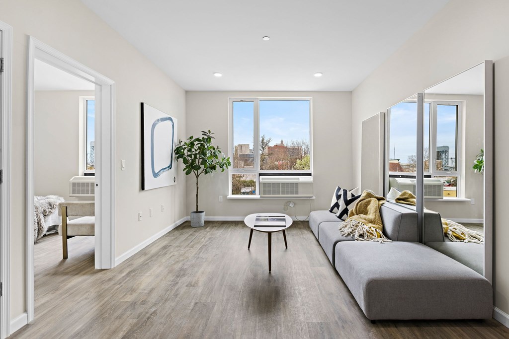 A living room with a grey couch, a coffee table, and a large window.