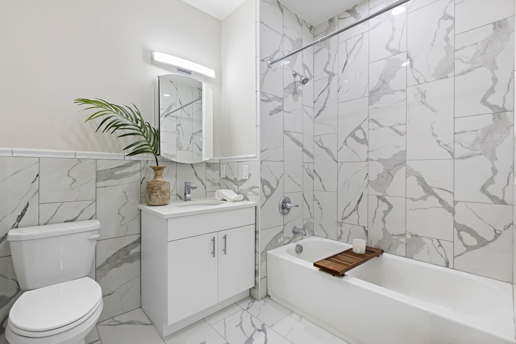 A white bathroom with a marble tile wall and a white bathtub.