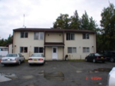 A building with a white door and windows with cars parked in front.