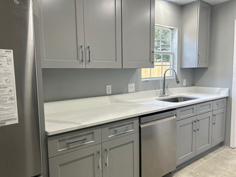 A kitchen with grey cabinets and a white countertop.
