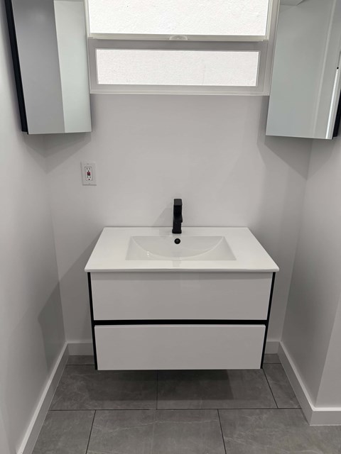 A white sink with a black faucet is in a white bathroom.