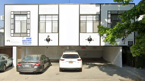 Two cars are parked in front of a white building with a sign that says "NOW SELLING".