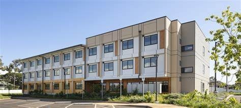 A modern building with a beige and white facade and a parking lot in front.