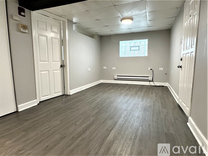 A room with wooden flooring and white walls, with a window and a door.