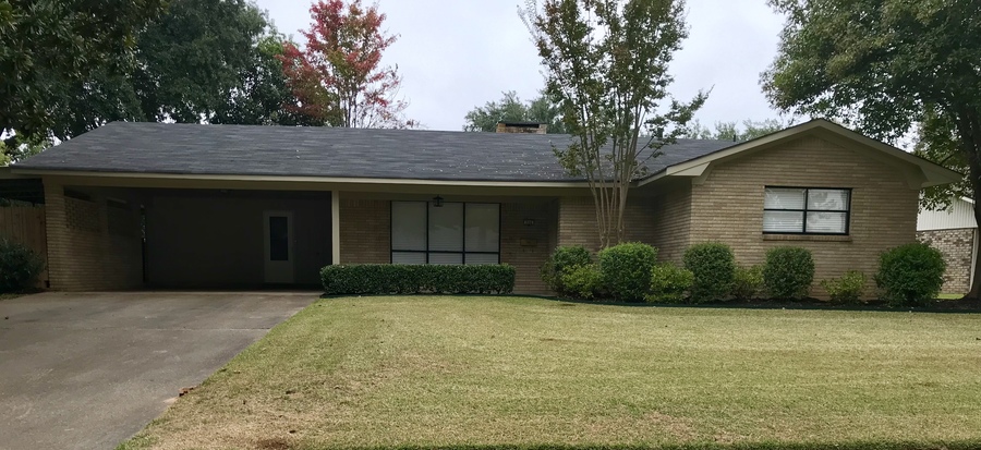 A house with a grey roof and a brown exterior with a green lawn in front.