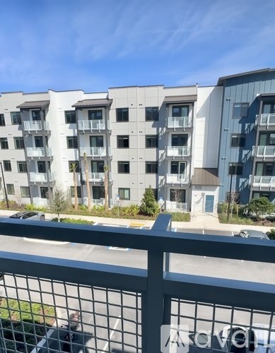 A row of modern apartment buildings with balconies and a fence in the foreground.