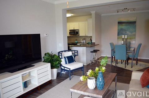 A living room with a television, a sofa, a coffee table, and a kitchen area in the background.