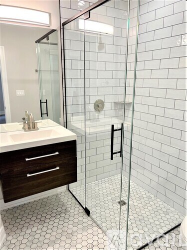 A white sink with a black handle is in a bathroom with a glass shower door.