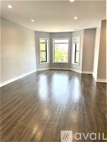 A spacious room with wooden flooring and two windows.