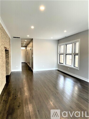 A spacious room with wooden floors and a large window on the right side.