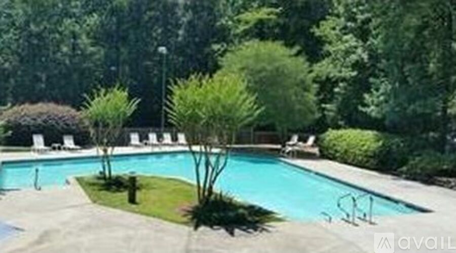 A pool surrounded by trees and lawn chairs.